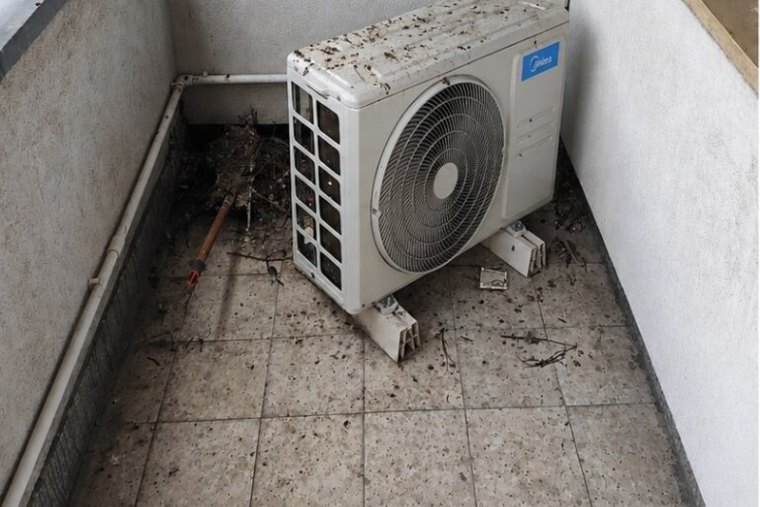 Balkon w krakowskim bloku przed sprzątaniem — liście, gałęzie i zabrudzona jednostka klimatyzacji